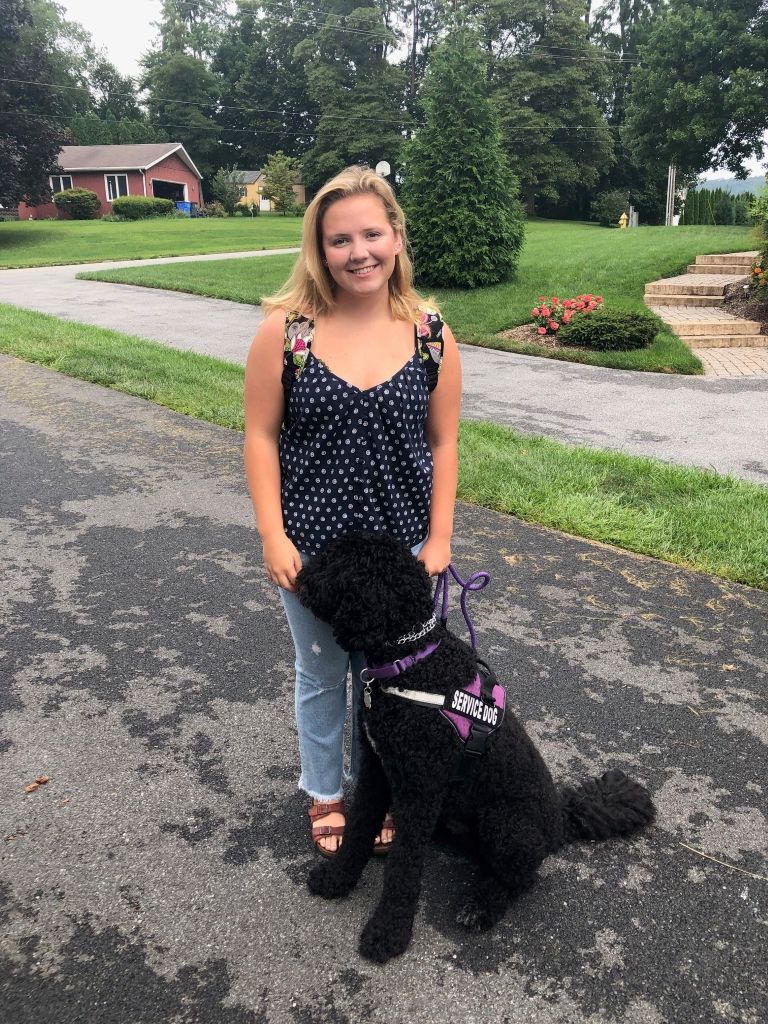 Megan with her black service dog wearing a purple service dog vest